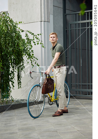 Handsome, stylish, young businessman in smart casual clothes standing near modern buildings with bike. Going to work 105095641