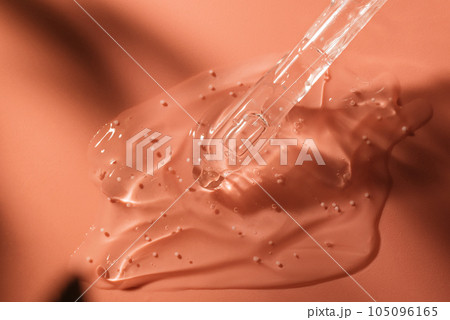 Beauty face serum gel with dropper. Transparent skincare cream with bubbles on coral background. Beauty face serum gel with dropper. Transparent skincare cream with bubbles on coral background. 105096165