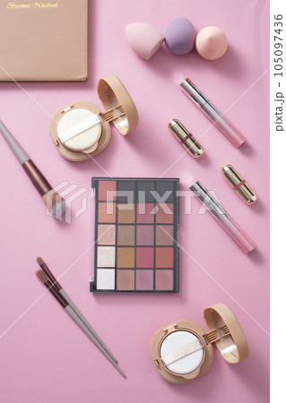 On a pastel pink background, makeup set: eyeshadow, lipstick, cushion, sponge and makeup brush creatively decorated. Concept for advertising cosmetic product, top view, flat lay 105097436