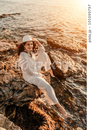 woman sea sunset. woman in a white pantsuit and hat is sitiing on the beach enjoying the sea. Happy summer holidays woman sea sunset. woman in a white pantsuit and hat is sitiing on the beach enjoying the sea. Happy summer holidays 105099797