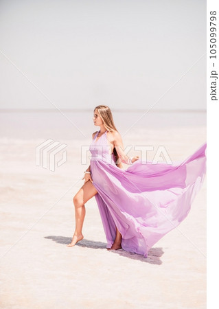 Woman pink salt lake. Against the backdrop of a pink salt lake, a woman in a long pink dress takes a leisurely stroll along the white, salty shore, capturing a wanderlust moment. 105099798