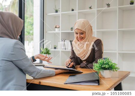Young muslim female business worker discussing with friends sitting together, working with tablet and financial documents at desk 105100085