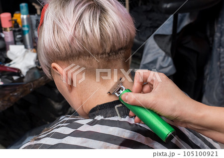 The hand of a woman of a professional barbershop worker trims the back of the head of a client with a trimmer at work The hand of a woman of a professional barbershop worker trims the back of the head of a client with a trimmer at work 105100921