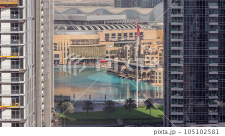 Aerial view of Dubai Fountain in downtown with palms in park next to shopping mall and souq timelapse, UAE 105102581