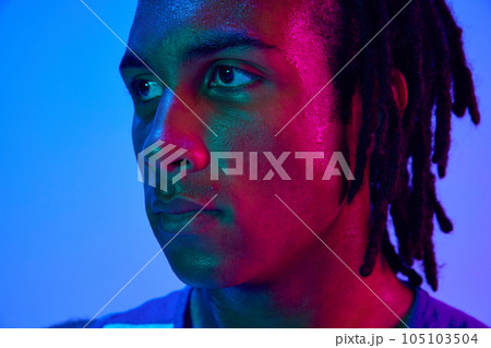Portrait of young man, professional athlete, basketball player posing against gradient blue background in neon lights 105103504