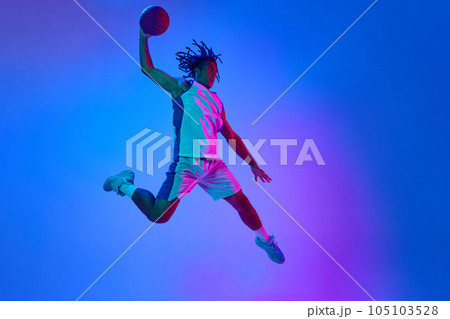 Competitive, ambitious sportsman, young basketball player in motion with ball against gradient blue background in neon lights Competitive, ambitious sportsman, young basketball player in motion with ball against gradient blue background in neon lights 105103528