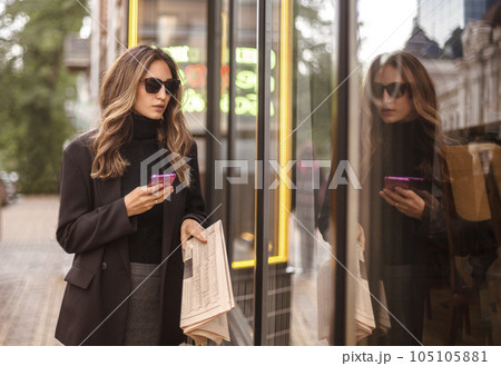 Young elegant fashionable woman looking in shop window while walking on city street on weekend Young elegant fashionable woman looking in shop window while walking on city street on weekend 105105881