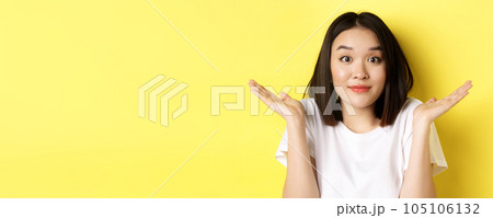 Silly mistake. Close up of cute asian girl saying sorry, shrugging shoulders and smiling with oops face expression, standing over yellow background Silly mistake. Close up of cute asian girl saying sorry, shrugging shoulders and smiling with oops face expression, standing over yellow background 105106132