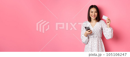 Attractive young asian woman order online, holding credit card and mobile phone, making internet purchase, standing happy over pink background Attractive young asian woman order online, holding credit card and mobile phone, making internet purchase, standing happy over pink background 105106247