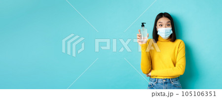 Covid-19, social distancing and pandemic concept. Cheerful asian woman showing hand sanitizer, recommend use antiseptic from coronavirus, wearing medical mask 105106351