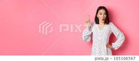 Excited asian girl having an idea, saying suggestion, raising finger and talking, standing over pink background 105106567