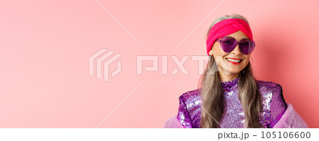 Fashion. Close up of stylish senior woman smiling happy at camera, wearing sunglasses and disco headband, pink background Fashion. Close up of stylish senior woman smiling happy at camera, wearing sunglasses and disco headband, pink background 105106600