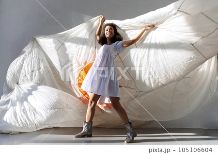 Young african american woman jumping with white fabric in white dress 105106604