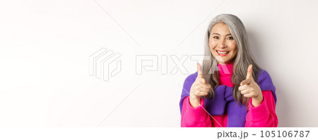 Beautiful and stylish asian grandmother pointing at camera, you can do this gesture, congratulating or praising, standing over white background 105106787