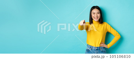 Beauty and fashion concept. Cheerful asian woman laughing and smiling, pointing finger at camera, choose you, standing over blue background 105106810