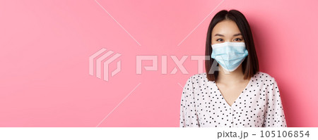 Covid-19, pandemic and lifestyle concept. Close-up of beautiful asian woman in face mask smiling with eyes, wearing protection from coronavirus in public, pink background Covid-19, pandemic and lifestyle concept. Close-up of beautiful asian woman in face mask smiling with eyes, wearing protection from coronavirus in public, pink background 105106854