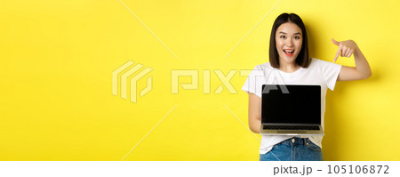 Young asian woman demonstrate online offer, showing laptop screen and smiling, standing over yellow background Young asian woman demonstrate online offer, showing laptop screen and smiling, standing over yellow background 105106872
