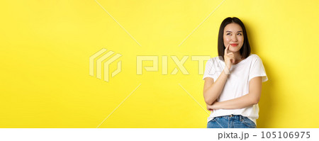 Beauty and fashion concept. Pensive asian woman thinking, looking thoughtful while pondering something, standing over yellow background Beauty and fashion concept. Pensive asian woman thinking, looking thoughtful while pondering something, standing over yellow background 105106975