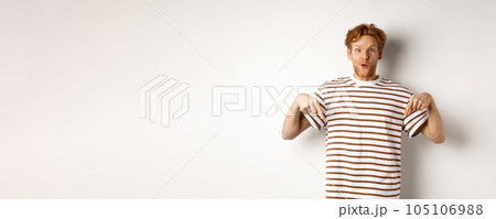 Image of funny redhead male student pointing fingers down, showing promo offer with excited smile, standing over white background 105106988