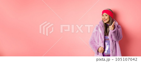 Fashion and shopping concept. Happy asian mature woman in stylish fake-fur coat pointing finger at camera, we need you gesture, standing over pin background Fashion and shopping concept. Happy asian mature woman in stylish fake-fur coat pointing finger at camera, we need you gesture, standing over pin background 105107042