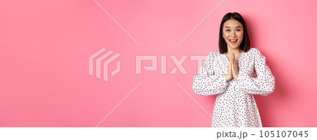 Beautiful asian woman thanking you, holding hands together in appreciation gesture, smiling happy at camera, standing grateful over pink background Beautiful asian woman thanking you, holding hands together in appreciation gesture, smiling happy at camera, standing grateful over pink background 105107045