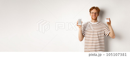 Shopping and finance concept. Young man showing blank mobile screen and plastic credit card, smiling at camera, white background 105107381