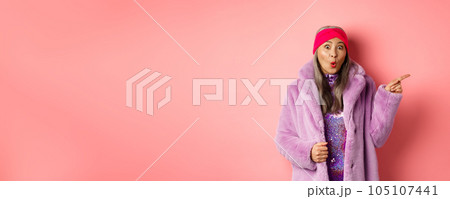 Cool asian granny pointing finger right and showing promo offer, checking out special deal on pink background Cool asian granny pointing finger right and showing promo offer, checking out special deal on pink background 105107441
