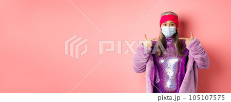Covid-19, social distancing and fashion concept. Asian edlerly woman in stylish party outfit and respirator, pointing fingers at face mask, asking to follow coronavirus quarantine rules Covid-19, social distancing and fashion concept. Asian edlerly woman in stylish party outfit and respirator, pointing fingers at face mask, asking to follow coronavirus quarantine rules 105107575