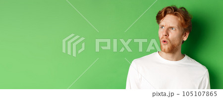 Confused redhead man staring left and looking worried, standing against green background Confused redhead man staring left and looking worried, standing against green background 105107865
