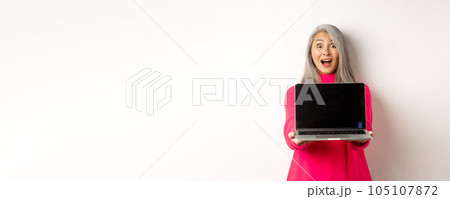 E-commerce concept. Amazed asian senior woman showing blank laptop screen and looking happy, demonstrating promo, white background 105107872