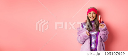 Cheerful asian senior woman having fun and partying, saying congrats or cheers as raising glass of champagne, smiling happy, standing over pink background Cheerful asian senior woman having fun and partying, saying congrats or cheers as raising glass of champagne, smiling happy, standing over pink background 105107999