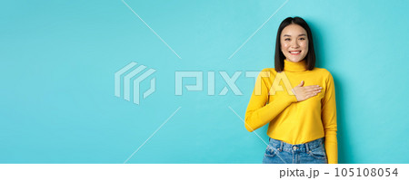 Image of proud smiling asian woman holding hand on heart, showing respect to national anthem, standing over blue background 105108054
