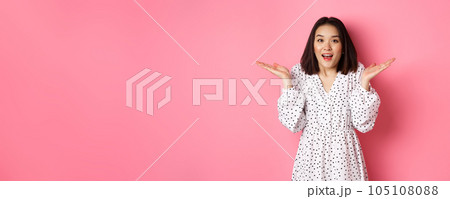Image of surprised korean girl in dress, female model staring at camera and gasping amazd, standing over pink background Image of surprised korean girl in dress, female model staring at camera and gasping amazd, standing over pink background 105108088