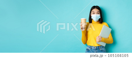 covid-19, health care and quarantine concept. Asian girl student in medical mask standing with laptop and coffee from cafe, standing over blue background covid-19, health care and quarantine concept. Asian girl student in medical mask standing with laptop and coffee from cafe, standing over blue background 105108105