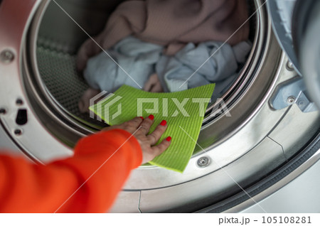 Woman washing dirty clothes, cleaning washing machine with rag in the laundry room. 105108281