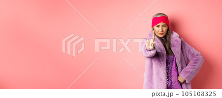 Fashion and shopping concept. Serious asian senior woman showing not so fast gesture, shaking extended finger to stop or warn you, looking determined at camera, wearing stylish purple clothes 105108325