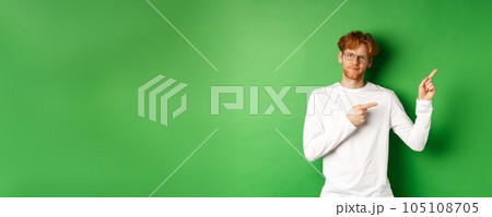 Skeptical caucasian man in glasses having doubts, pouting and frowning while pointing fingers right at something bad, standing over green background Skeptical caucasian man in glasses having doubts, pouting and frowning while pointing fingers right at something bad, standing over green background 105108705