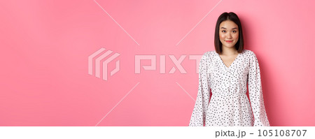 Beautiful asian lady smiling at camera, wearing cute romantic dress, standing over pink background Beautiful asian lady smiling at camera, wearing cute romantic dress, standing over pink background 105108707
