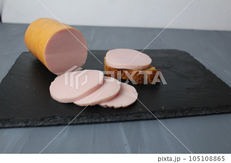 Boiled children's sausage for sandwiches Narean into pieces on a black board with green basil 105108865
