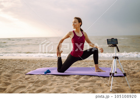 Online training. Sporty woman yoga coach records video online training on beach. Sport, Blogging. Online training. Sporty woman yoga coach records video online training on beach. Sport, Blogging. 105108920