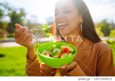 Healthy lifestyle. Young woman eating fresh vegetable salad on sunny day outdoor. Vegetarian. 105109021