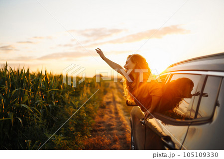 Happy woman outstretches her arms while sticking out car window. Lifestyle, travel, tourism, nature. 105109330