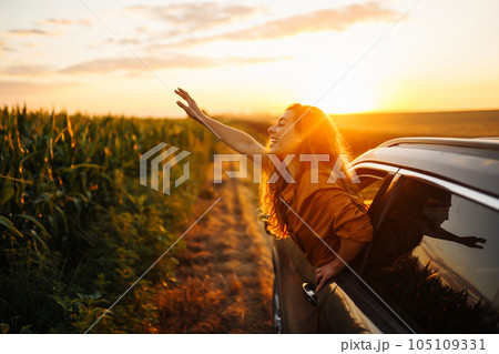Happy woman outstretches her arms while sticking out car window. Lifestyle, travel, tourism, nature. 105109331