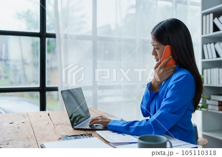 Busy businesswoman wearing a suit busy with work workaholic while sitting at work clear paperworks with documents and talk on the phone on your smartphone hear the hustle and bustle, busy concepts 105110318