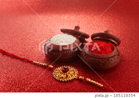 Raksha Bandhan. Rakhi string, Rice Grains and Kumkum on red background. 105110354