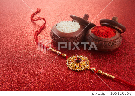 Raksha Bandhan. Rakhi string, Rice Grains and Kumkum on red background. 105110356