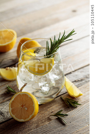 Gin tonic with ice, rosemary, and lemon slices on an old wooden table. Gin tonic with ice, rosemary, and lemon slices on an old wooden table. 105110445
