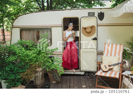 Happy hippie girl are having a good time with cup of tea in camper trailer. Holiday, vacation, trip concept. 105110761