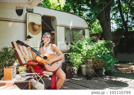 Happy hippie girl is having a good time with playing on guitar in camper trailer. Holiday, vacation, trip concept. Happy hippie girl is having a good time with playing on guitar in camper trailer. Holiday, vacation, trip concept. 105110799