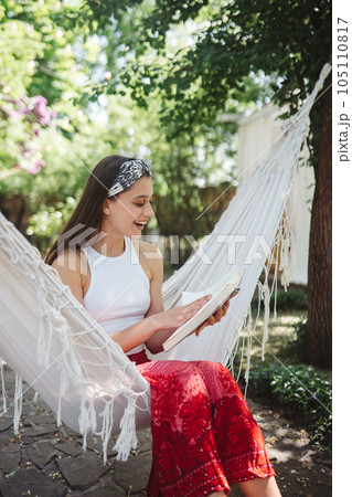 Happy hippie girl is reading a book in hammock having a good time in camper trailer. Holiday, vacation, trip concept. Happy hippie girl is reading a book in hammock having a good time in camper trailer. Holiday, vacation, trip concept. 105110817